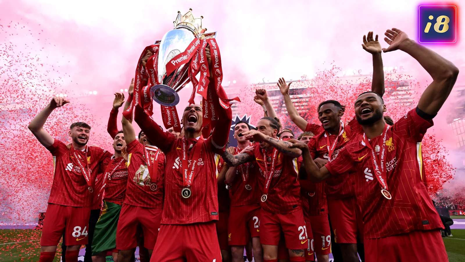 Soccer team in red jerseys celebrates a victory, lifting a trophy. Red confetti fills the stadium background, creating a jubilant scene.